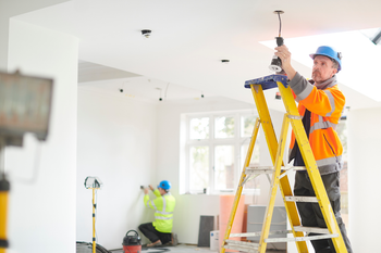 A man is standing on a ladder installing a light fixture.
