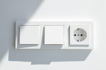 A white light switch and socket on a white wall.
