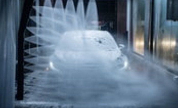 Car being washed in a car wash, water spraying over the vehicle, creating a misty effect.