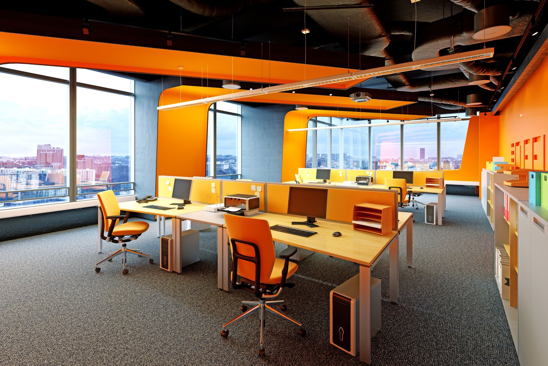 Modern office lounge with desks, chairs, computers, and large windows overlooking a cityscape