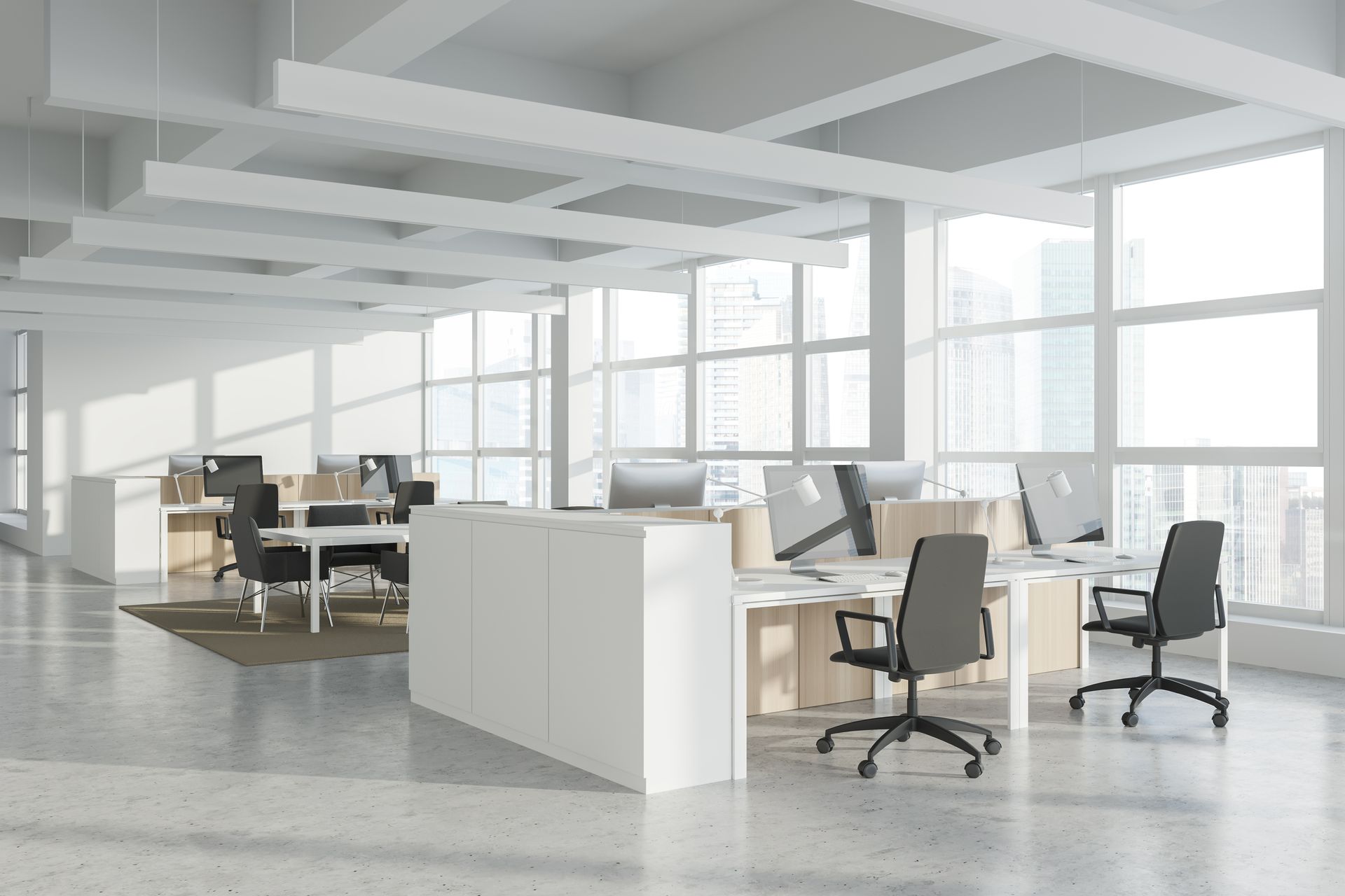 Modern open office with desks, chairs, computers, and large windows in bright daylight