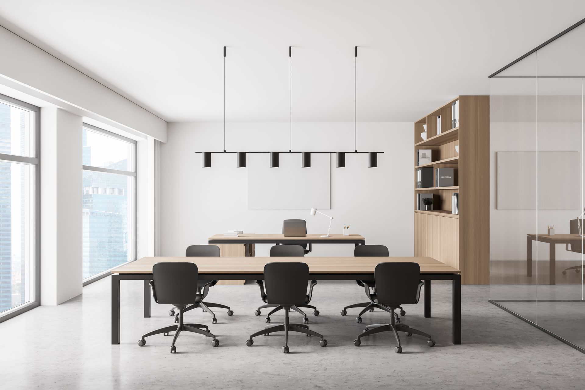 Modern open office meeting room with long tables, black chairs, hanging lights, and large windows.