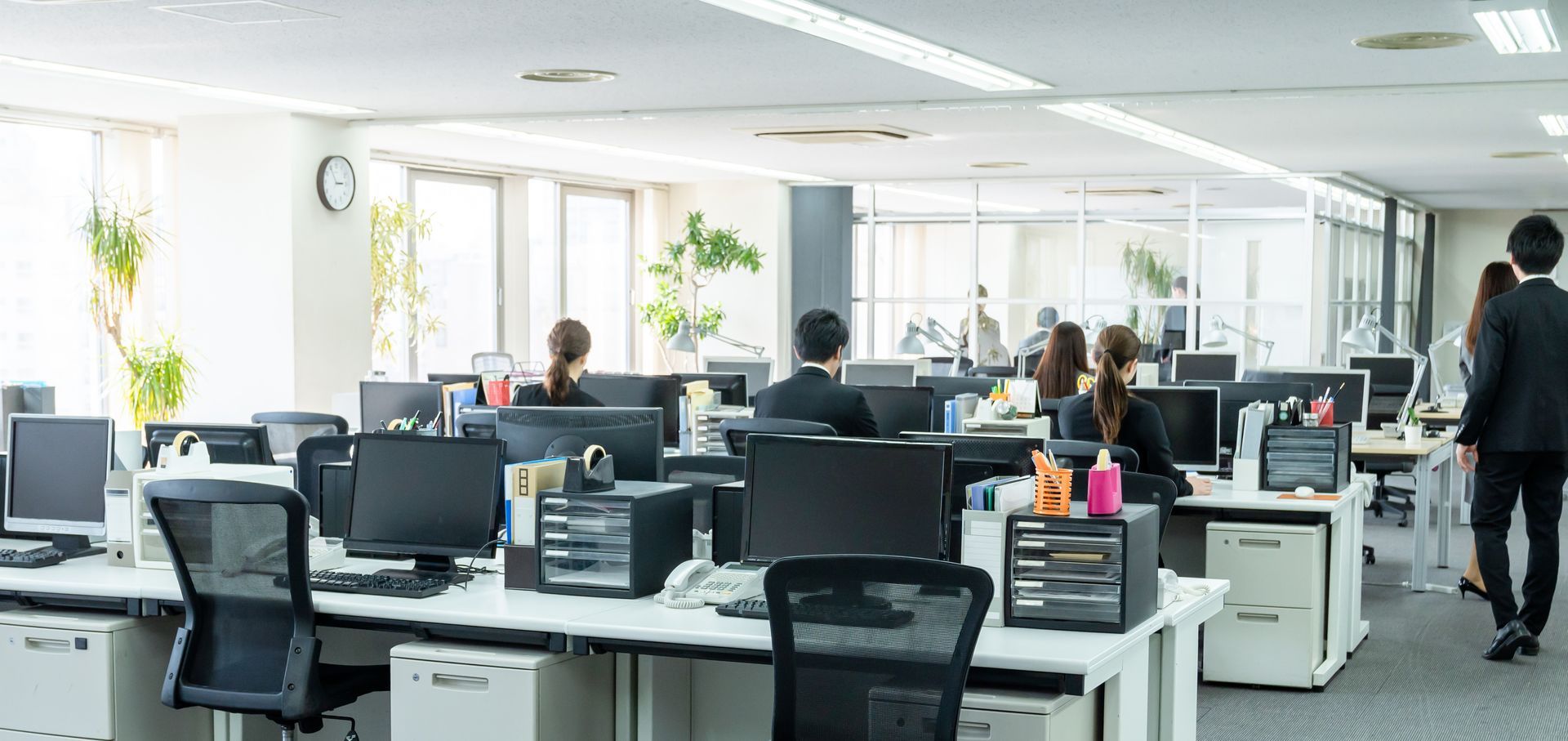 Bright open-plan office with desks, computers, and several people working