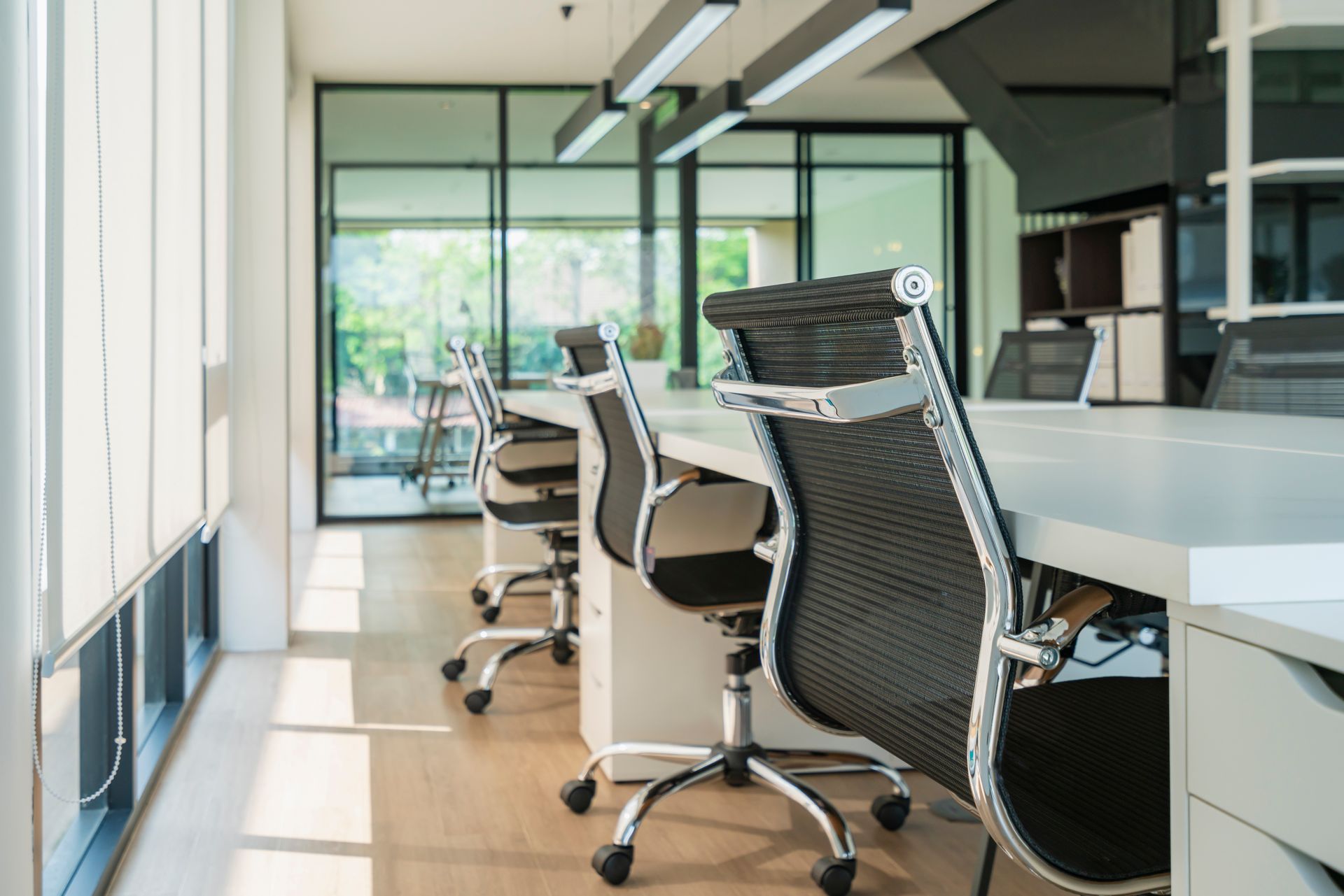 Modern office with rows of wheeled chairs beside desks and large windows overlooking greenery