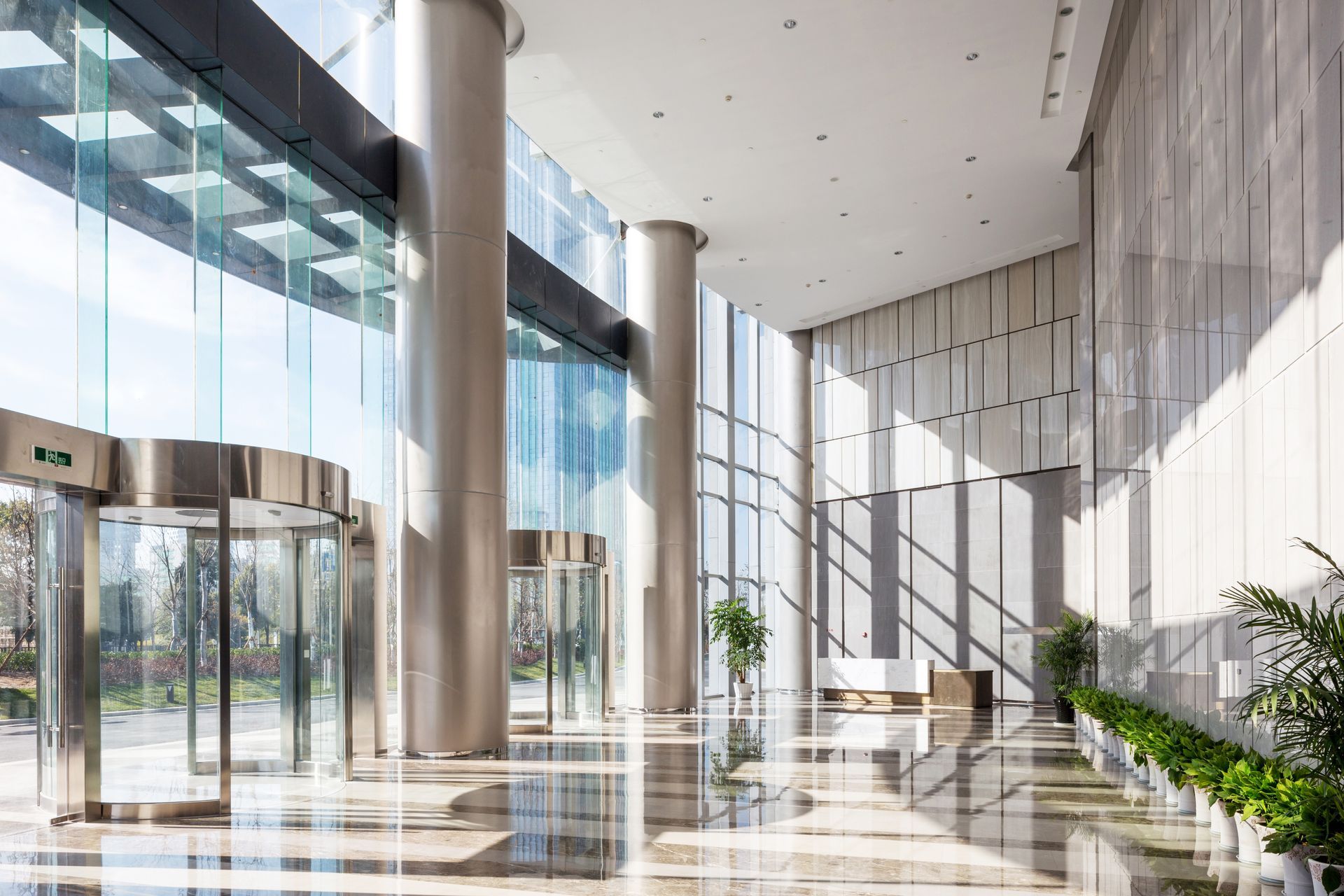 Bright modern glass lobby with tall columns, polished floors, and sunlight streaming in through large windows