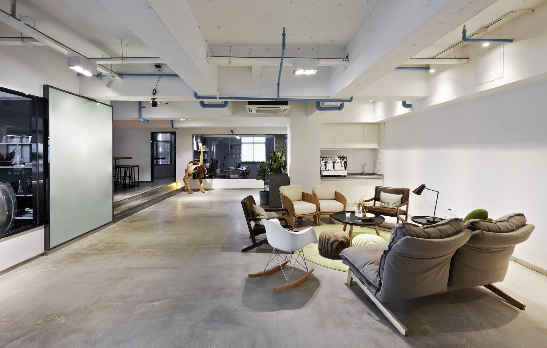 Modern open office with desks, black chairs, large windows, and gray carpet flooring
