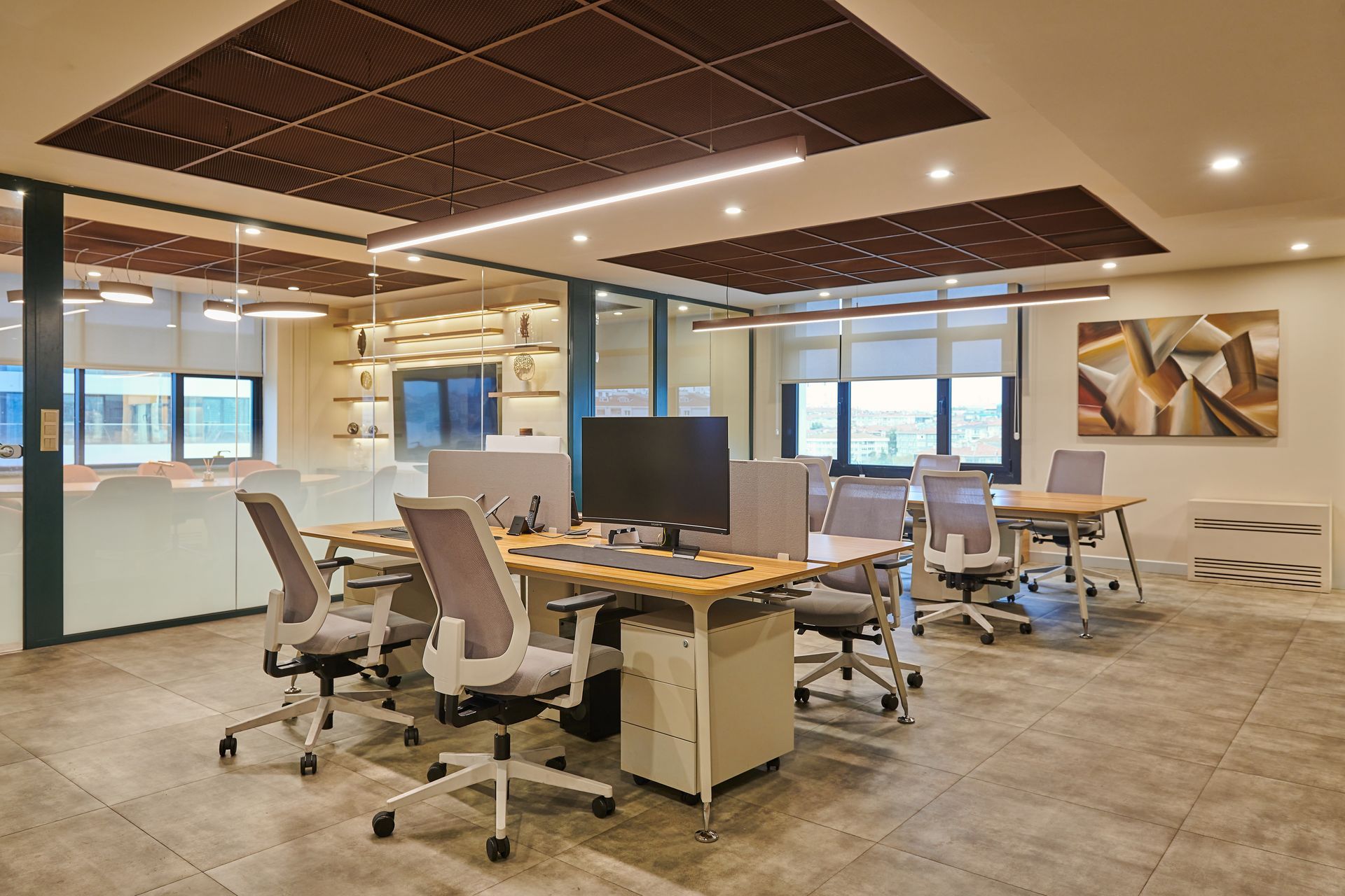 Modern open-plan office with desks, rolling chairs, computer monitors, and large windows