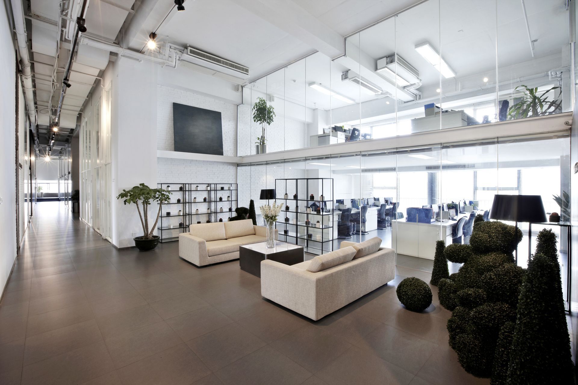 Modern white office lounge with sofas, glass walls, plants, and loft-style lighting