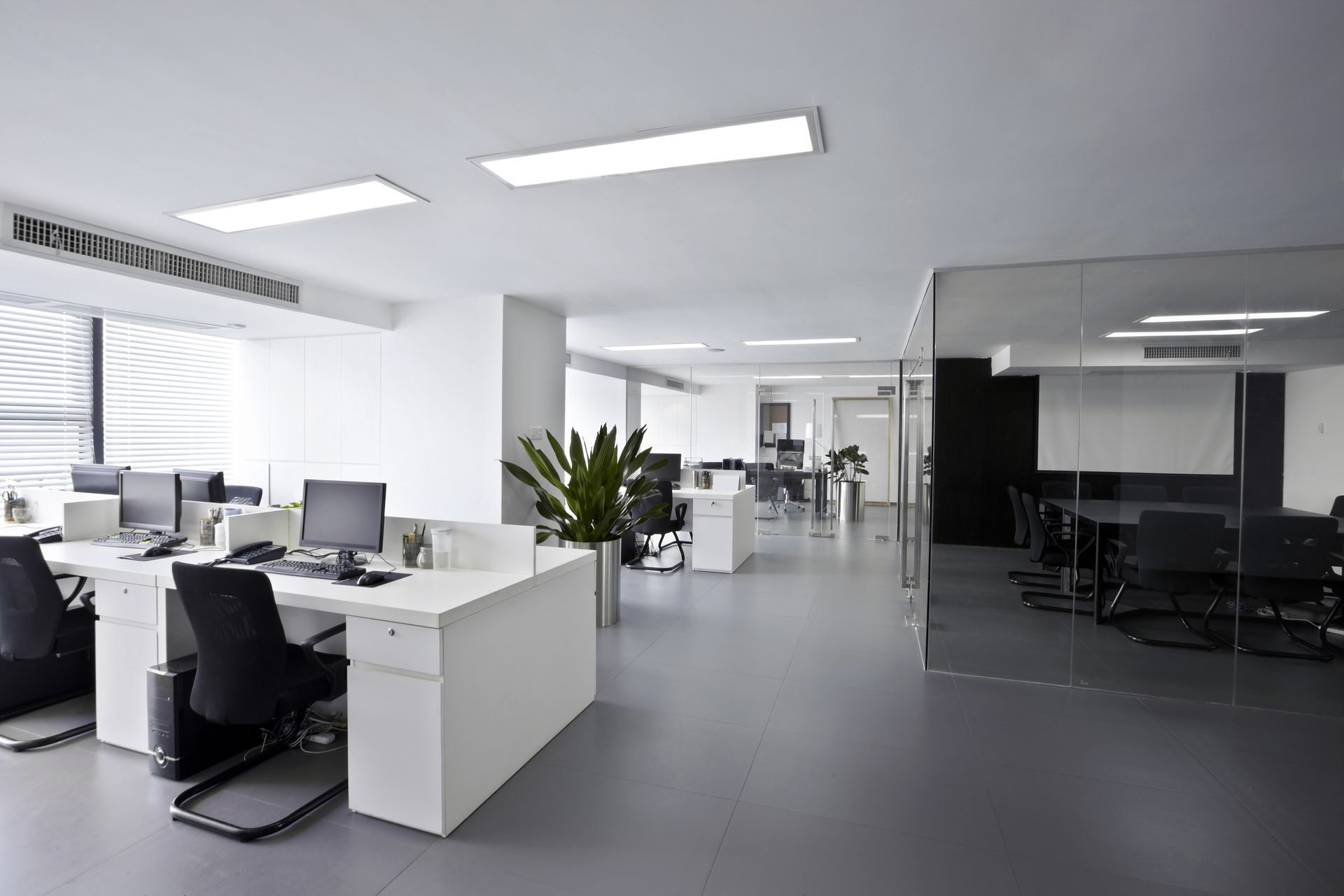 Bright, modern open-plan office with desks, computers, and a black conference area.