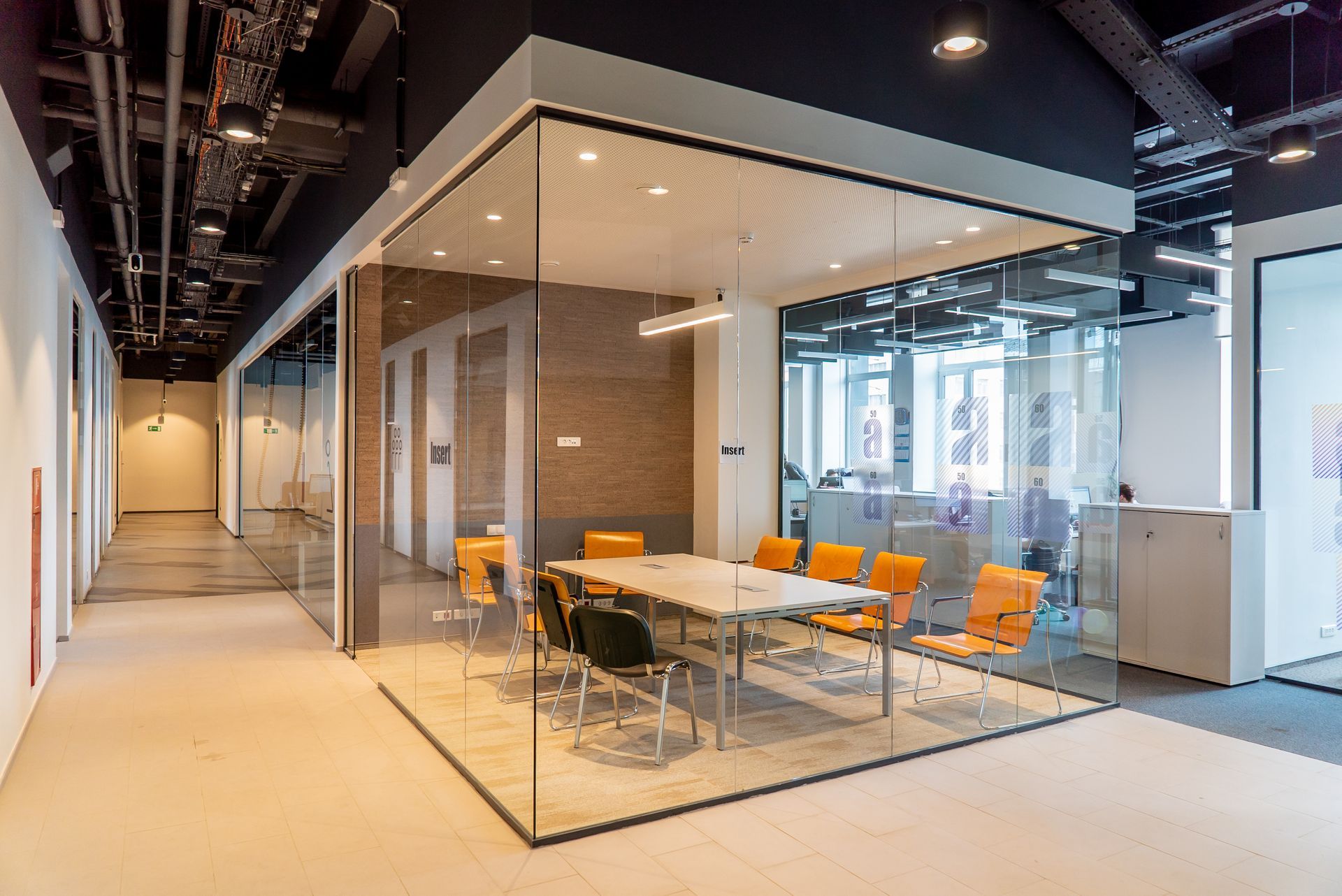 Glass-walled office meeting room with orange chairs in a modern hallway