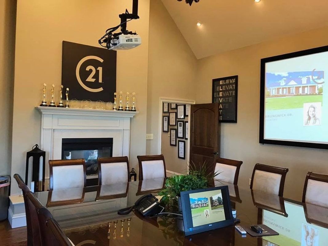 Conference room with white fireplace, chairs, wall-mounted screen, and table displaying a laptop.