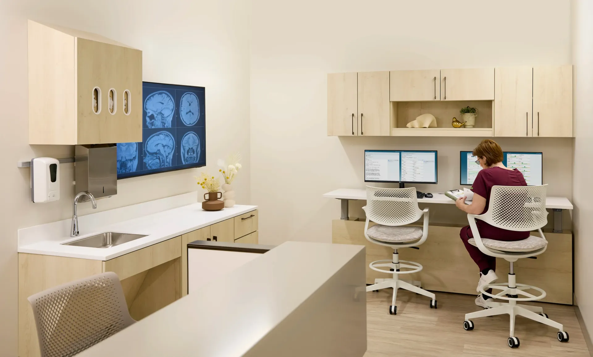 Modern dental office with a clinician working at dual computer monitors beside an exam chair