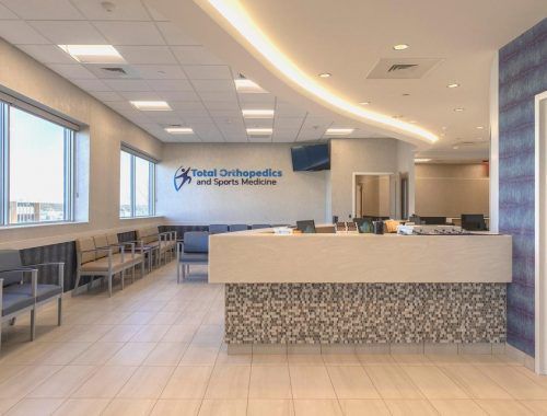 Dental clinic reception area with waiting chairs, front desk, and tiled floors under bright ceiling lights