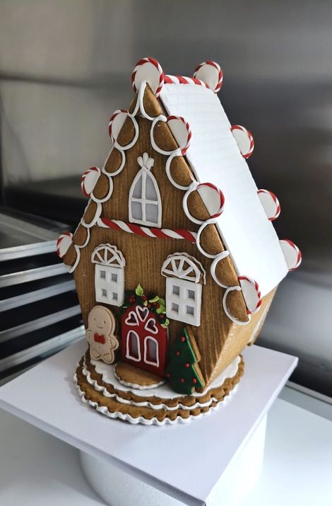Casetta di pan di zenzero con tetto di glassa bianca, decorata con biscotti, su un'alzata per torte bianca.