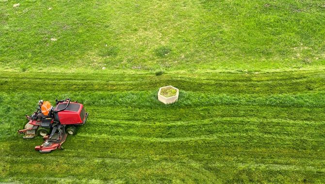 Worker mowing a grassy field beside a white bucket