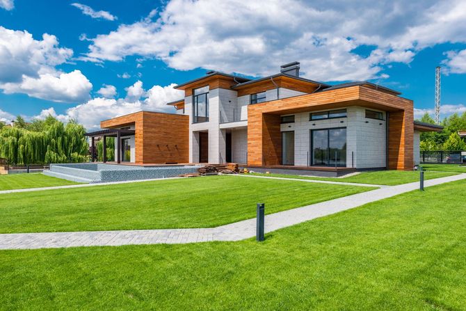 Modern luxury house with wood and white exterior, large windows, and a green lawn under a blue sky
