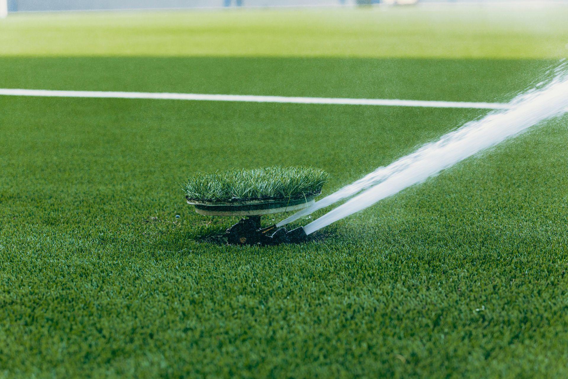 Lawn sprinkler watering green grass on a sports field