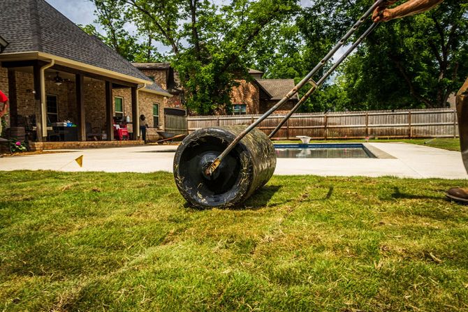 Lawn mower cutting grass in a backyard near a patio and swimming pool