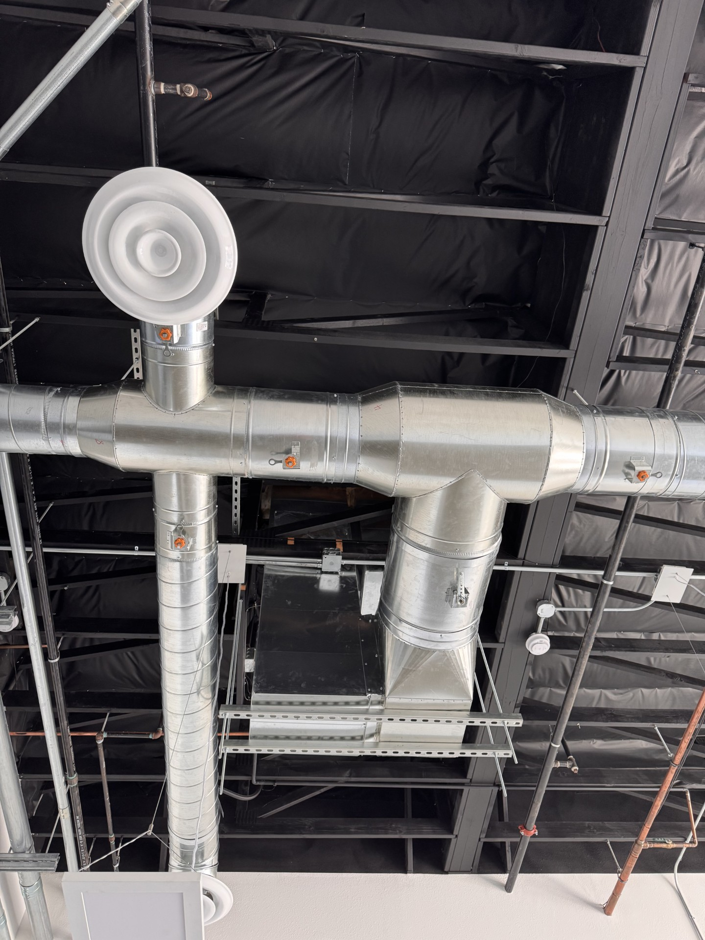 Air ducts in an attic, with blue light shining through a window in the background.