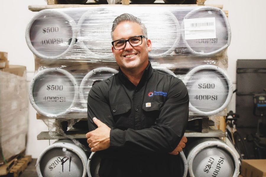 Man in glasses smiling, arms crossed, stands before a stack of industrial gas cylinders.
