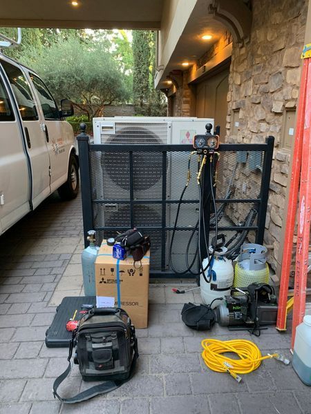 HVAC technician's tools near a white van and an outdoor AC unit behind a black metal fence.
