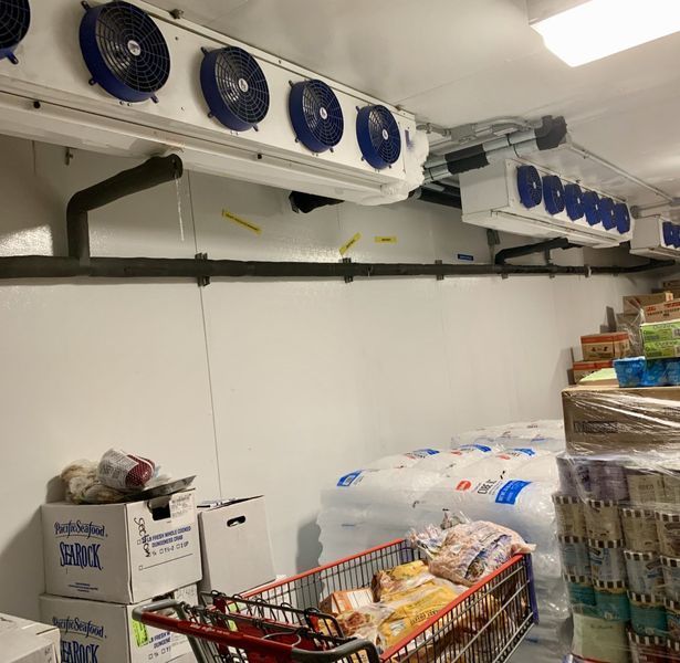 Interior of a cold storage room with ceiling-mounted refrigeration units, filled with grocery items and a shopping cart.
