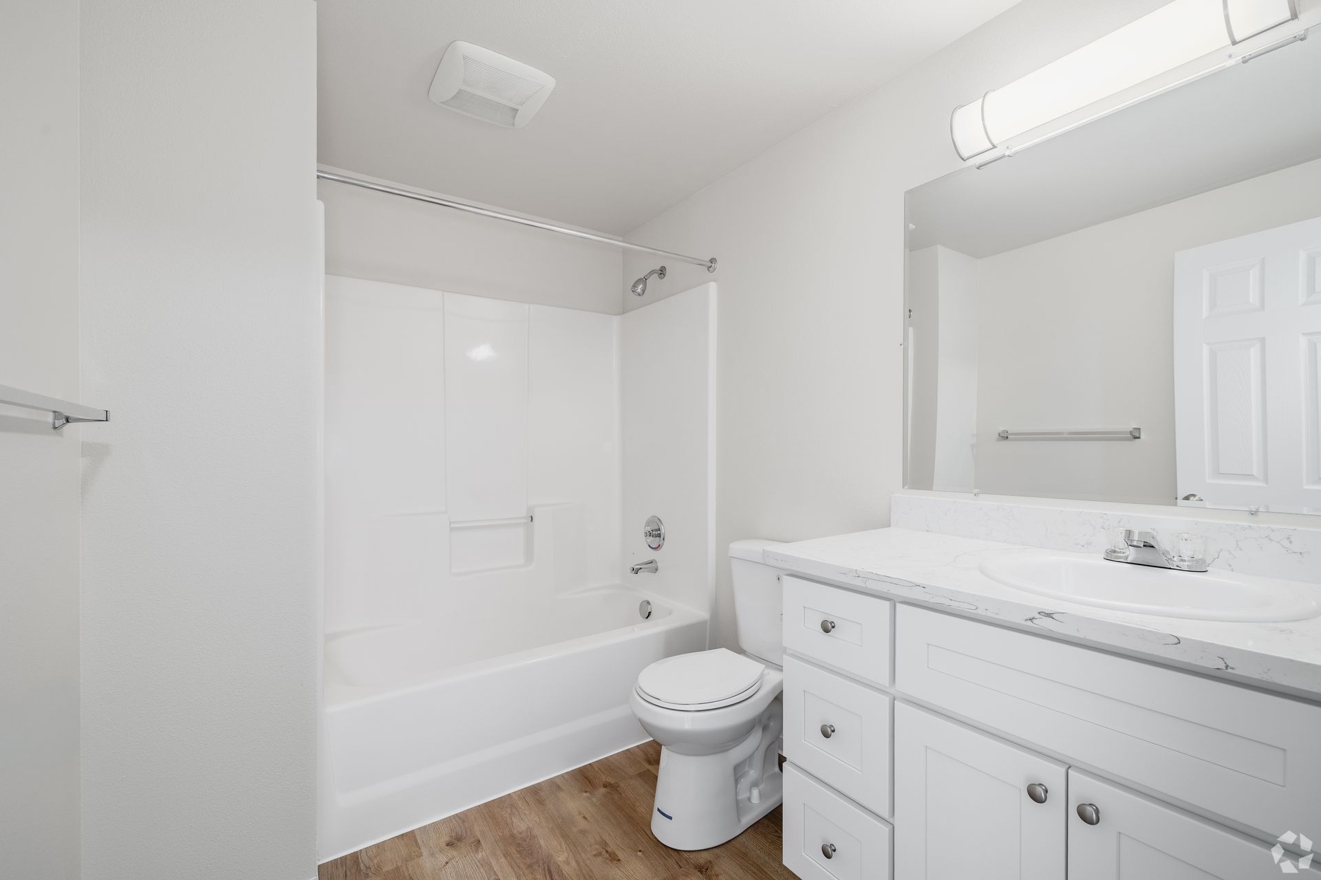 Bright white bathroom with tub, toilet, vanity, and large mirror