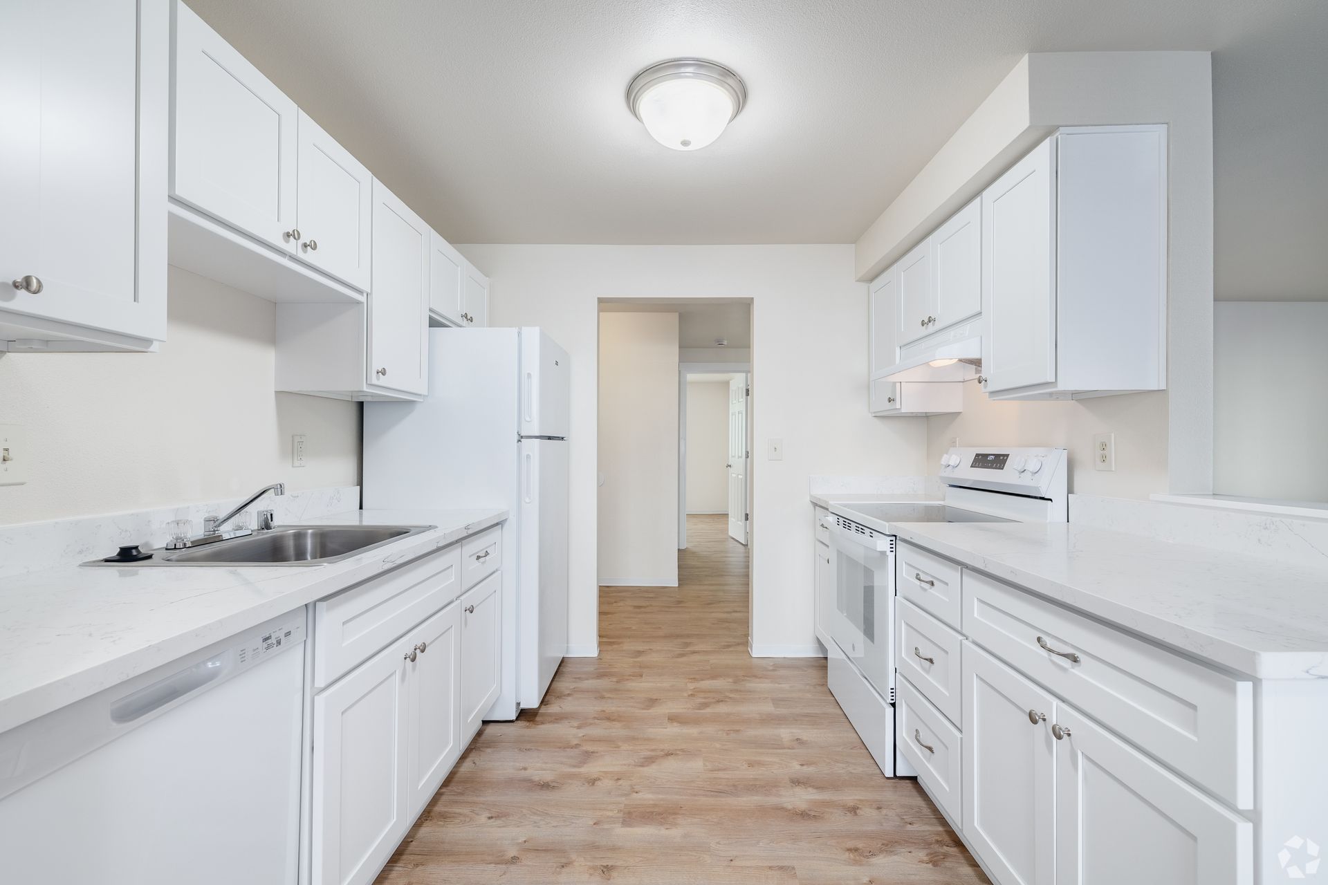 Bright white galley kitchen with wood floors, cabinets, counters, and a refrigerator.
