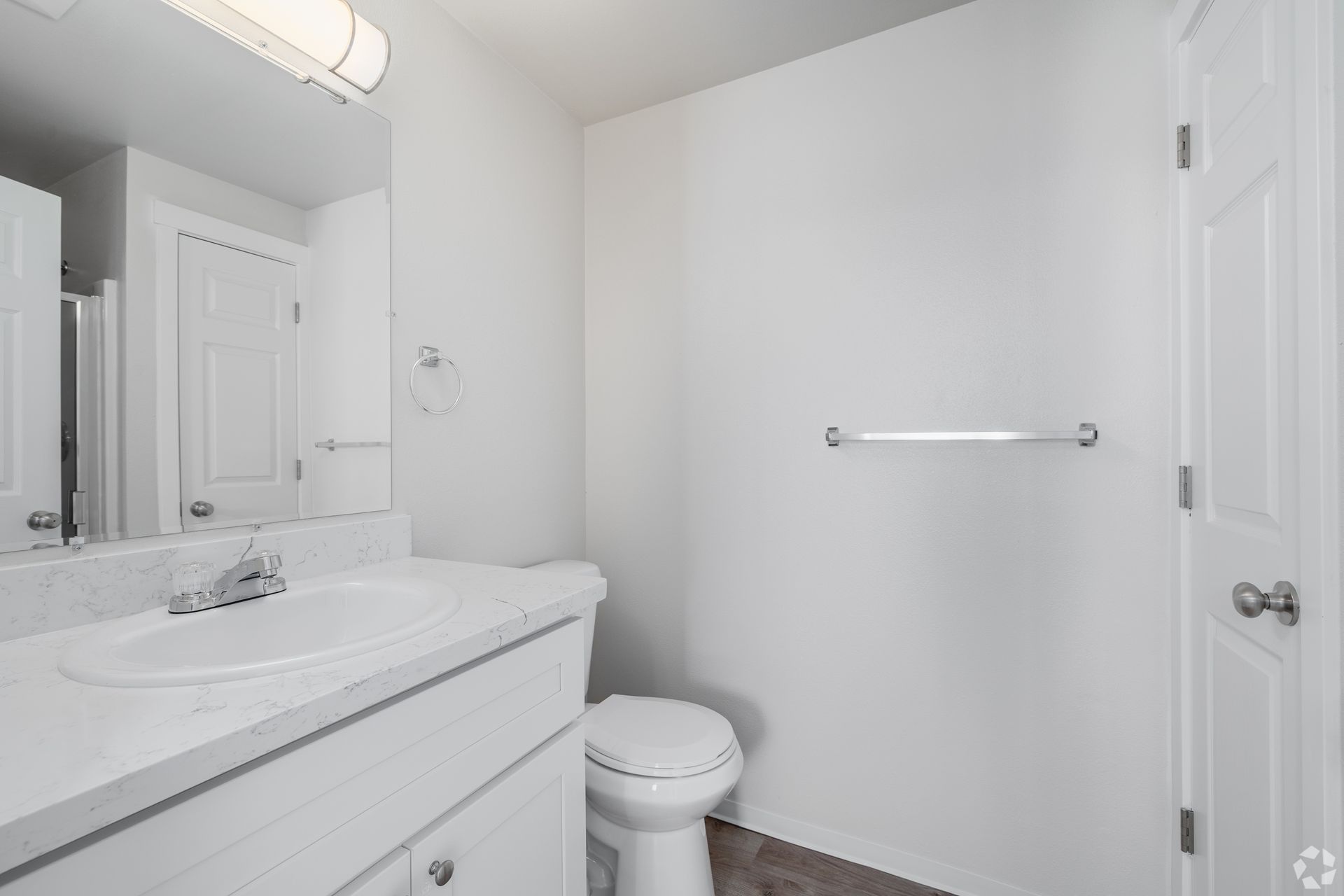 Bright white bathroom with vanity, toilet, mirror, and towel bar.