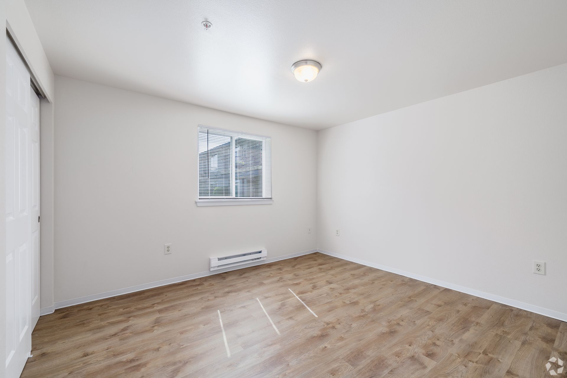 Empty white bedroom with wood floors, window, and ceiling light