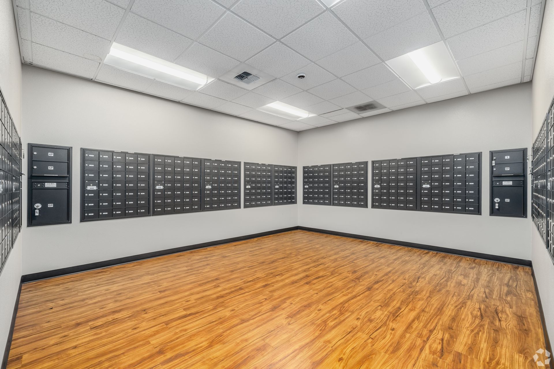 Empty room with wood floor and gray walls lined with mailboxes
