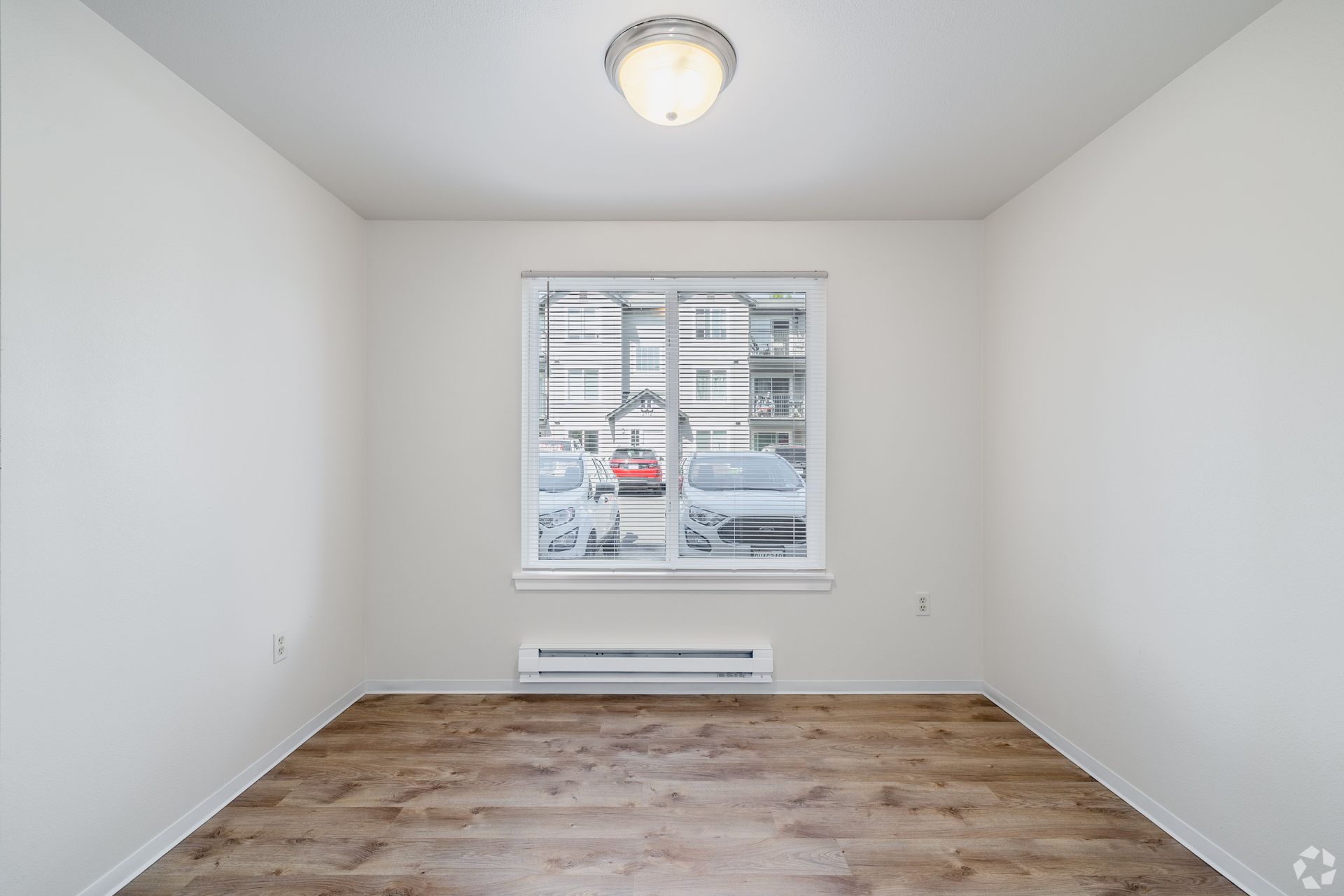 Empty white room with wood floor, centered window, and ceiling light