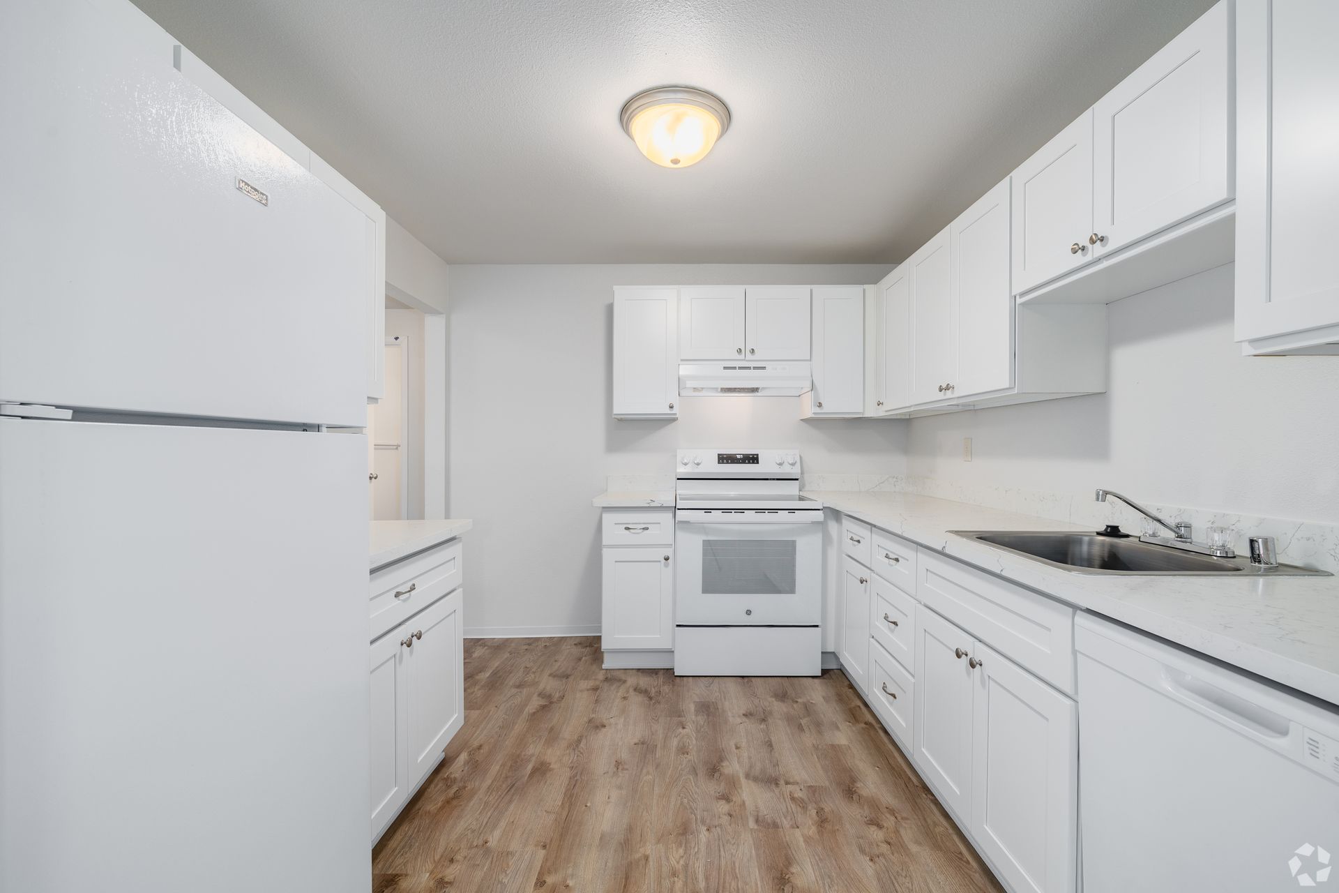 Bright white kitchen with wood floor, white cabinets, stove, and sink along one wall