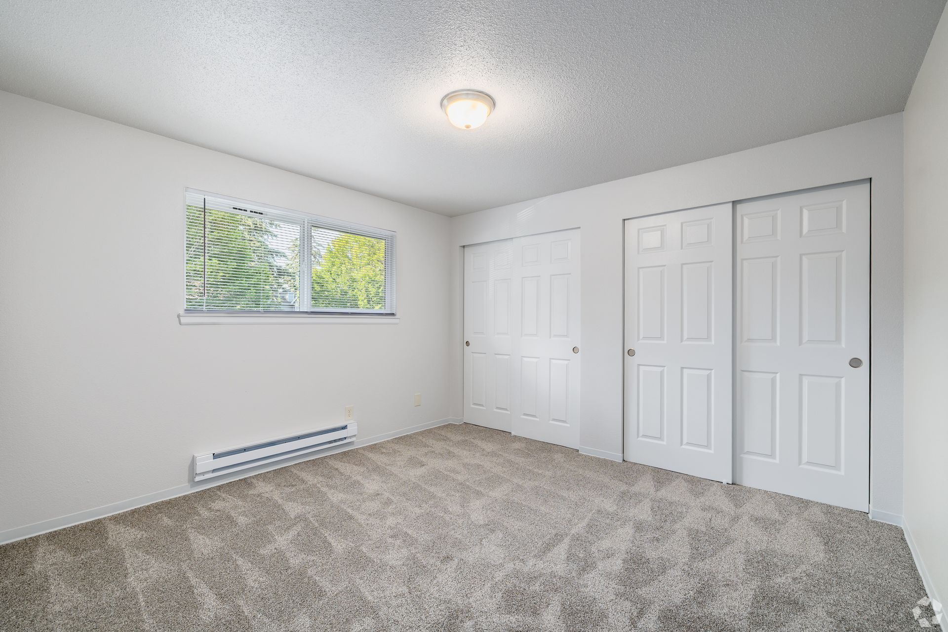 Empty white bedroom with carpet, window, ceiling light, and double closet doors
