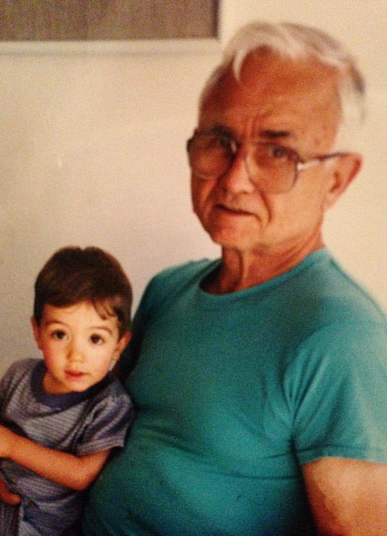 Older man in a teal shirt holding a toddler, both facing the camera indoors