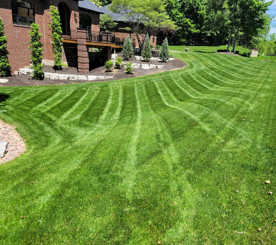 A lush green lawn is being mowed in front of a brick house.