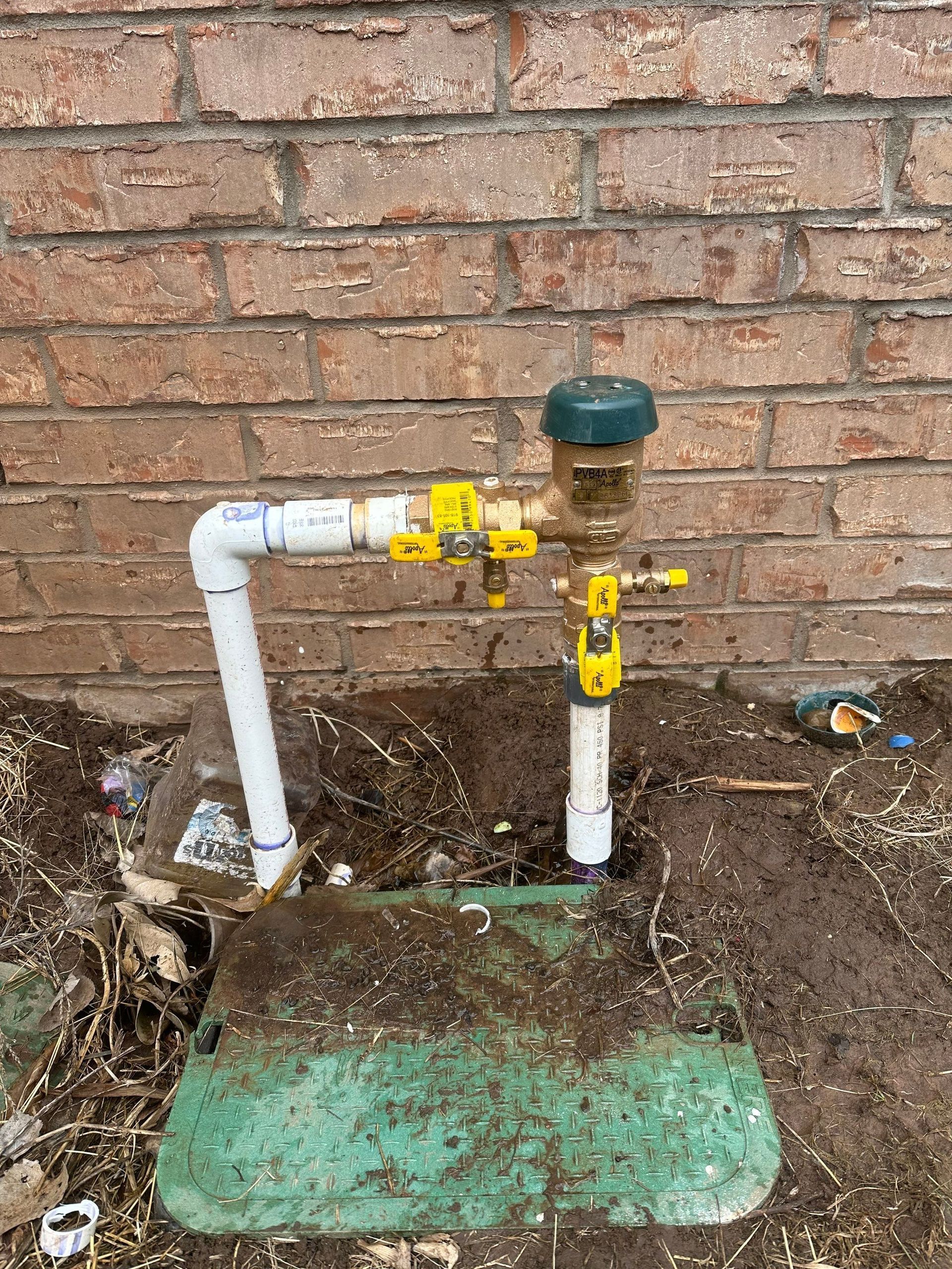 A sprinkler is sitting in the dirt next to a brick wall.