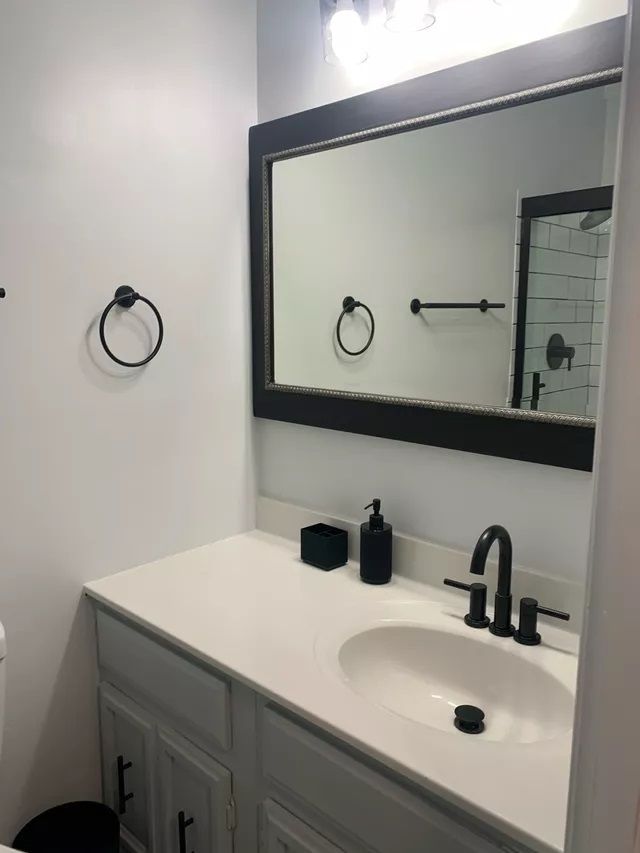 Bathroom with white countertop, black fixtures, large mirror, and gray cabinet.