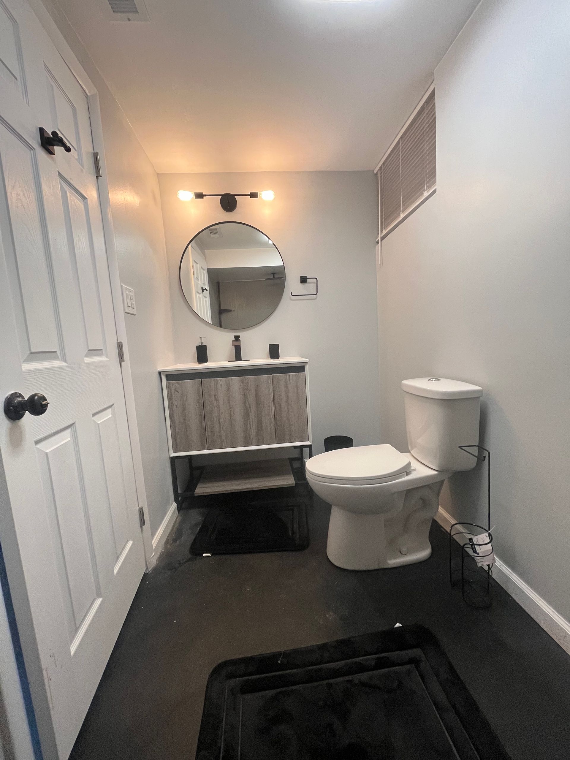 Small bathroom with a vanity, toilet, and door; gray walls, dark floor, and black accents.