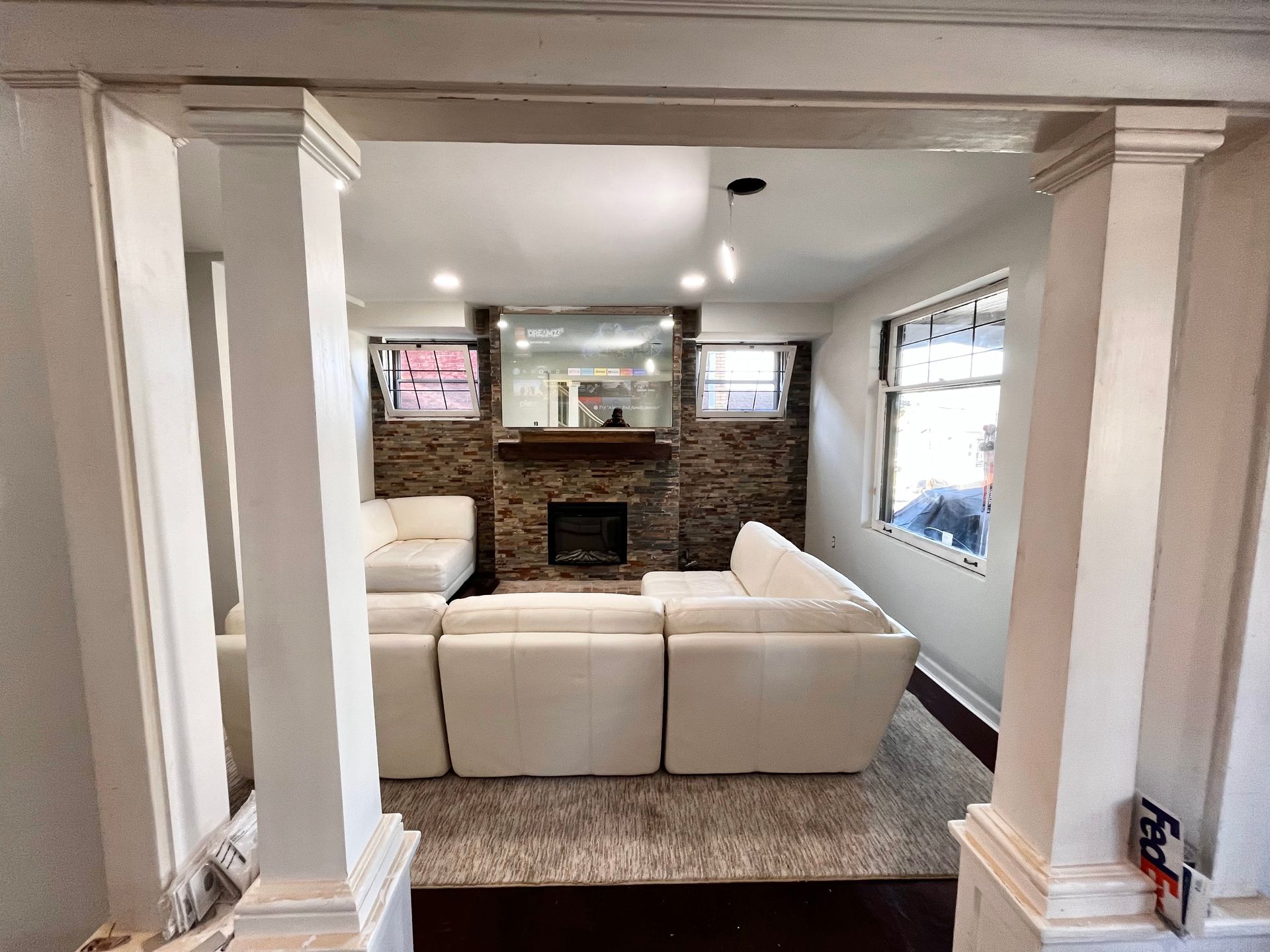 Living room with white sectional sofa, fireplace, stone wall, columns, and light fixtures.