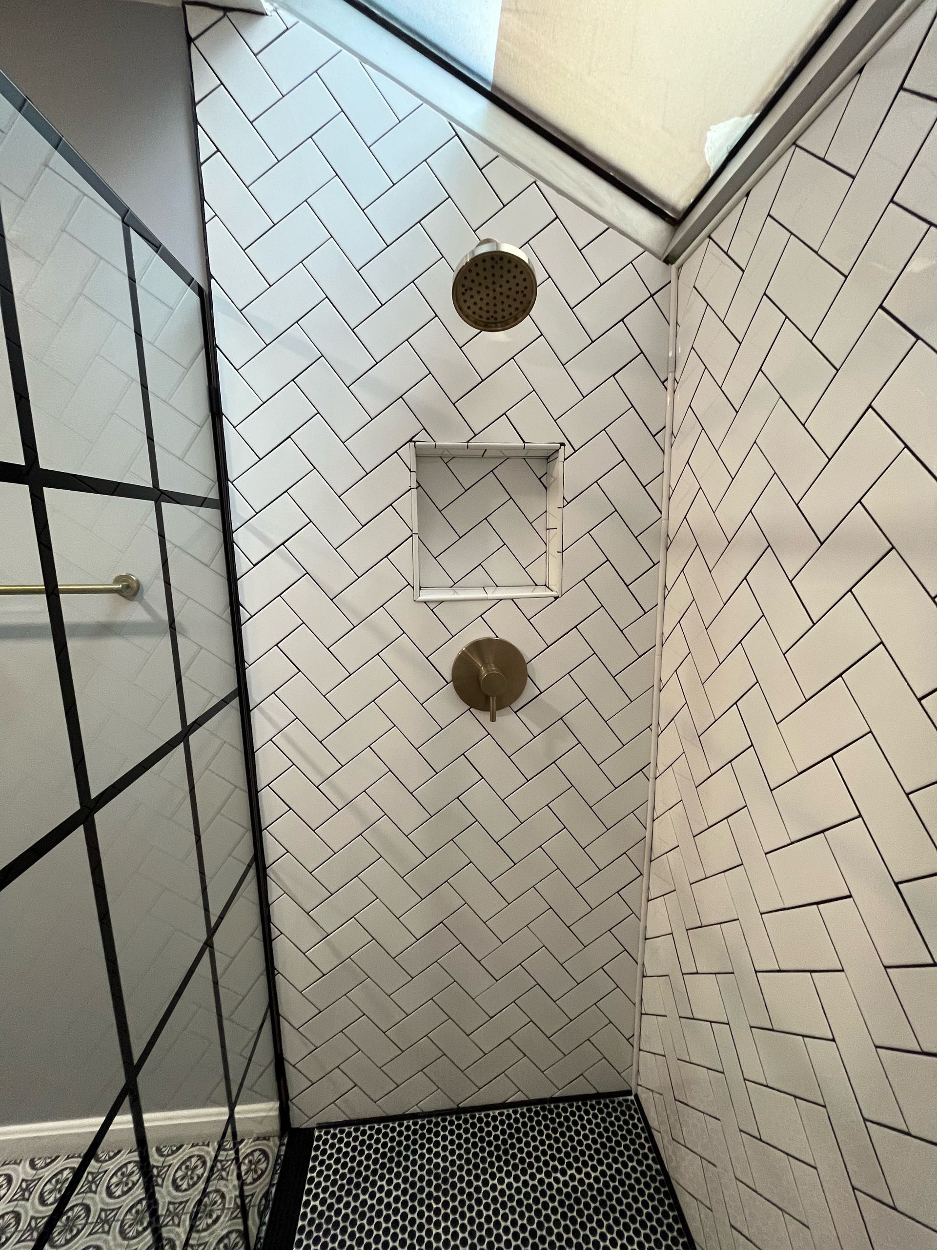 Shower interior with white herringbone tile, gold fixtures, and patterned floor.