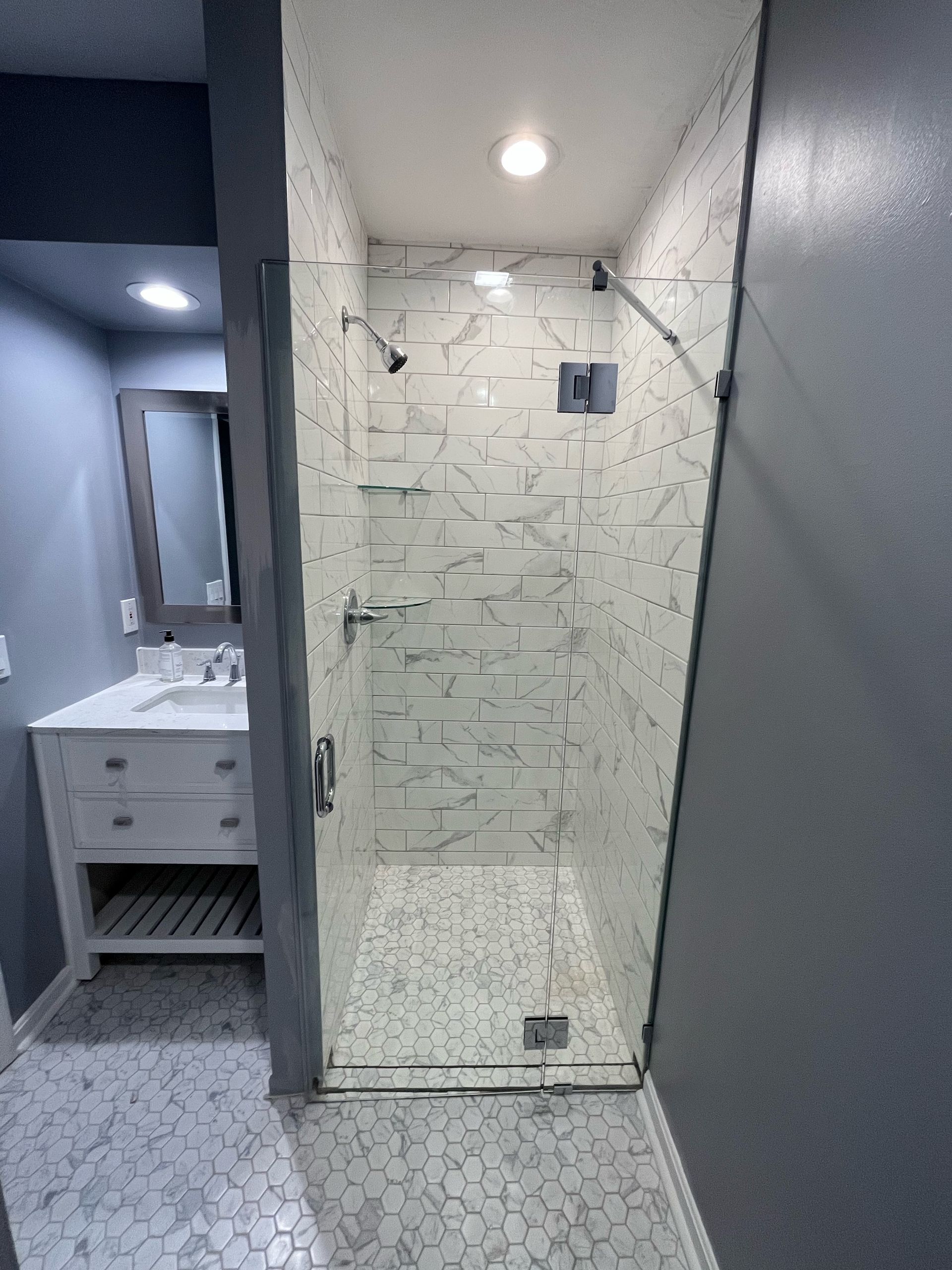 Bathroom with glass shower, white textured tile, and gray walls.
