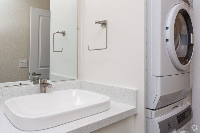 Modern bathroom with sink, mirror, and stacked washer and dryer beside it