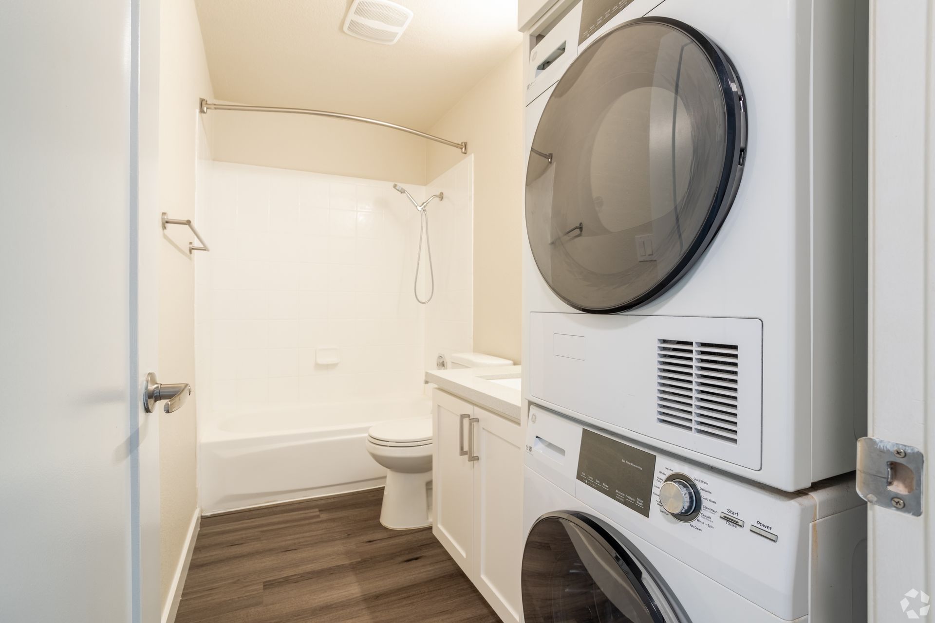 Small white laundry room and bathroom with stacked washer-dryer and toilet in a compact space