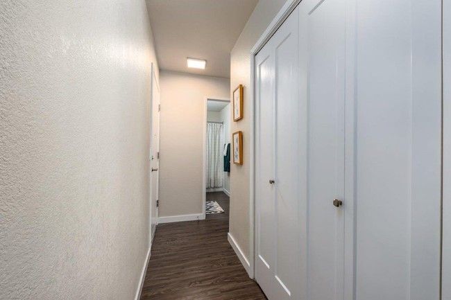 Narrow hallway with white walls, dark wood floor, and white closet doors leading to a room ahead