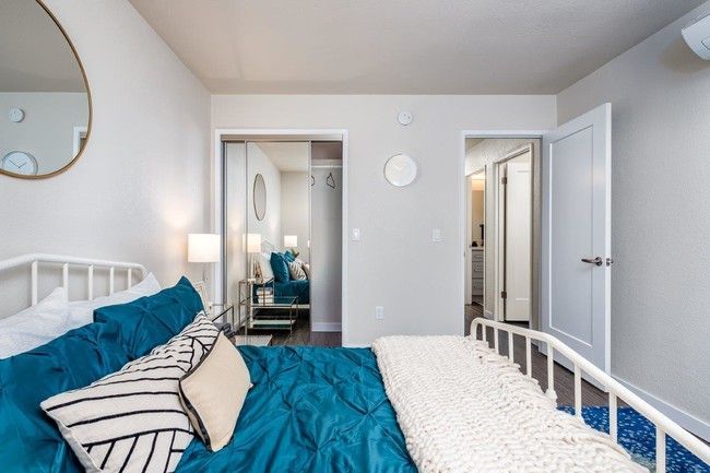 Bright bedroom with teal bedding, white walls, and an open closet and doorway in the background
