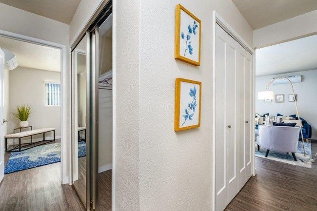 Bright hallway with framed art, open closet, and view into a dining room and bedroom beyond.