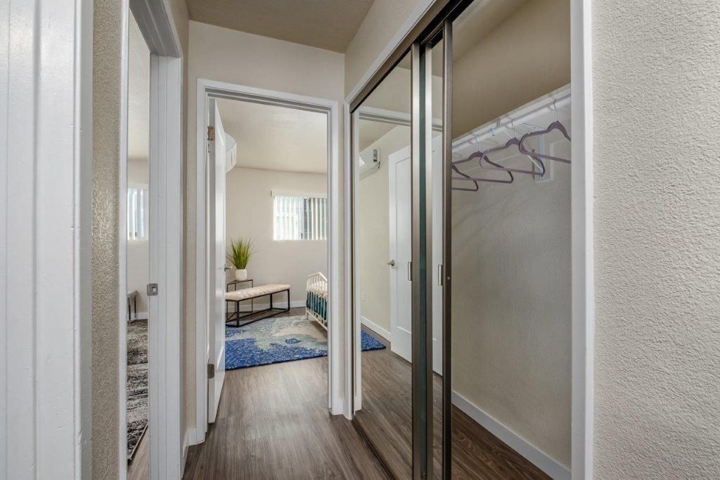 Bright hallway with mirrored closet doors leading to a bedroom with a blue rug and small plant table