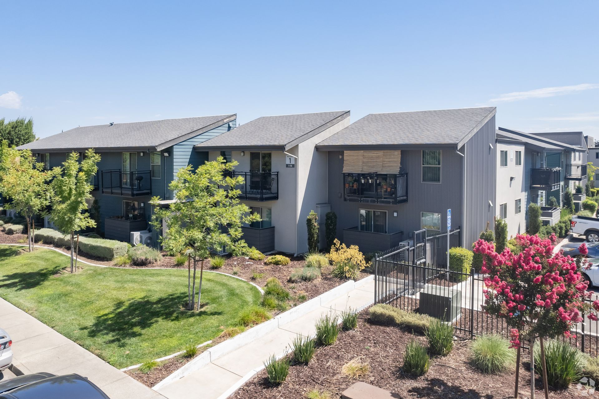 Row of modern apartment townhouses with balconies, green lawns, and flowering shrubs on a sunny day