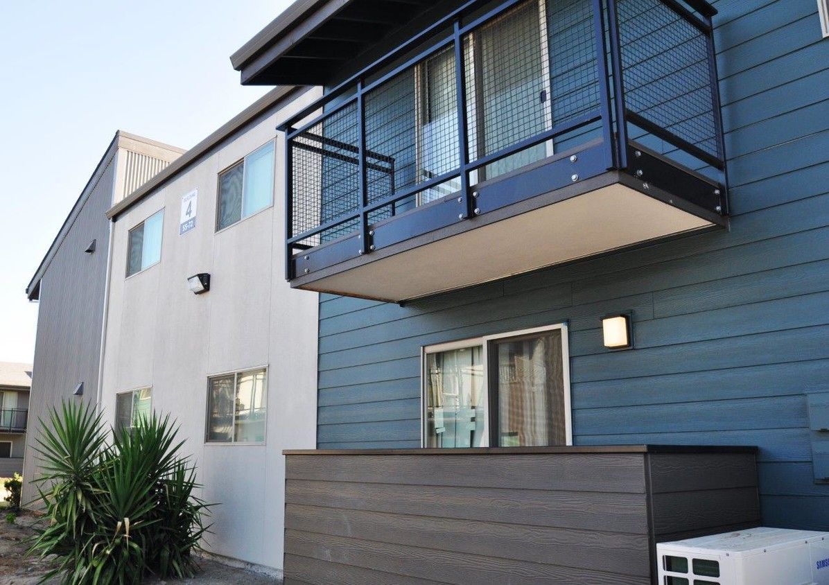 Apartment building exterior with blue and gray siding and a small balcony